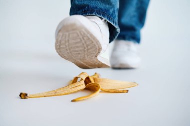 Beyaz arka planda muz kabuğuna basmak, kaza, komik bir kavram.