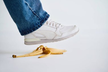 Beyaz arka planda muz kabuğuna basmak, kaza, komik bir kavram.