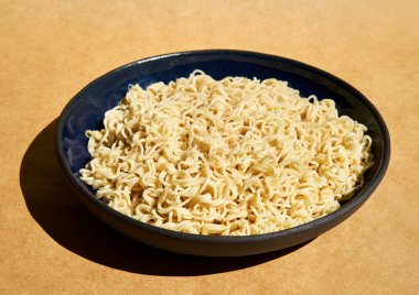 Kahverengi arka planda seramik tabakta servis edilen hazır erişteler. Basit yemek konsepti.