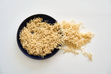 Pişmiş erişteler taşar ve beyaz arka planda dolu kaseden masaya dökülür.