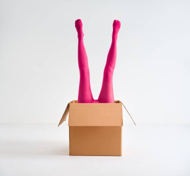 Beyaz stüdyo arka planında açık karton kutudan yükselen parlak pembe taytlı kadın bacakları.
