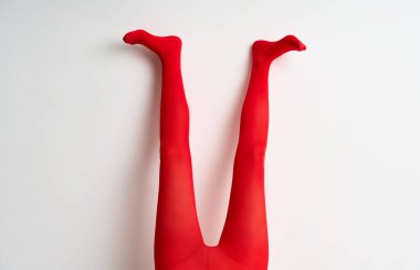 Uzun ince bacakları olan kırmızı taytlı bir kadın beyaz duvar arkasında poz veriyor..