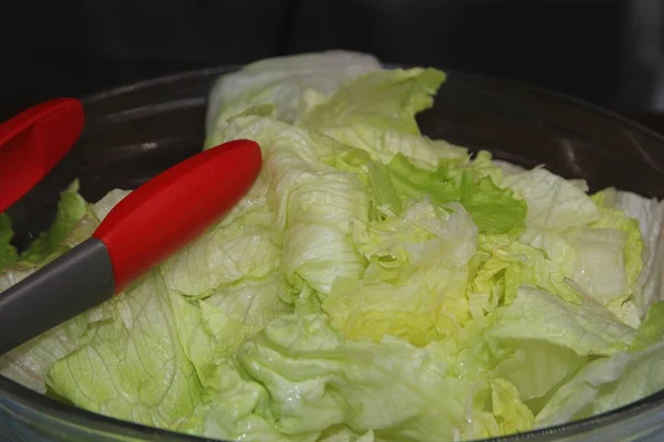 Shredded lettuce on a clear bowl with red-tipped tongs