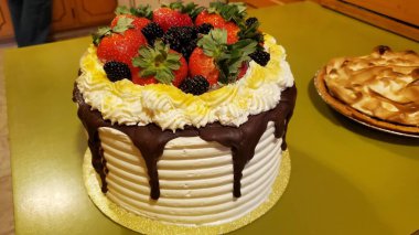 Beyaz ve sarı krema ve çikolata damlalarıyla süslenmiş çilek ve böğürtlenlerle süslenmiş bir pastanın yan görüntüsü