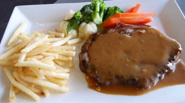 Soslu biftek, yanında sebze ve patates kızartması.