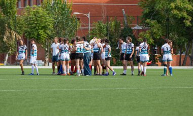 Madrid, Espaa, 13-10-2023. Canlı bir öğleden sonra ışığında, bir kadın üniversitesi ragbi takımı sahada bir oyunu kutluyor.