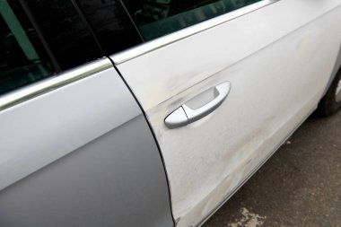 Silver car with white door after a crash accident. Side impact. Poor quality painting. Wrong color car's door. Painted over dent on a car's body. Bad repair concept photo. Closeup.
