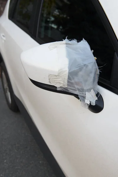 墜落したサイドミラー付きの白い車 テープで恐ろしい自己修復 バンダリズムのコンセプト写真 垂直写真のクローズアップ — ストック写真