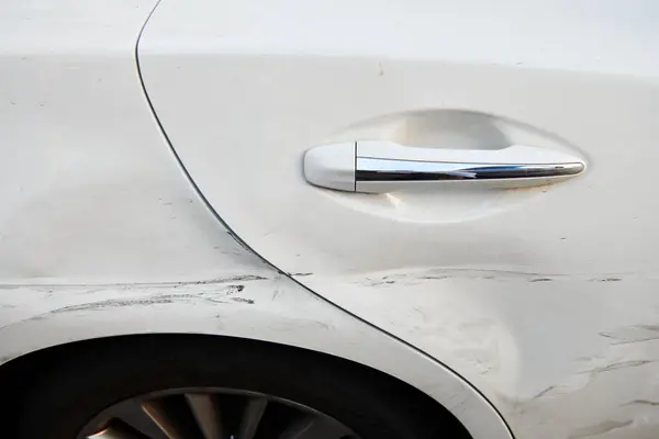 White car after crash accident. Door of luxury car with scratches and dents. Insurance case. Closeup. Horizontal photo.