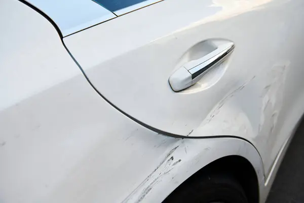 White car after crash accident. Door of luxury car with scratches and dents. Insurance case. Closeup. Horizontal photo.