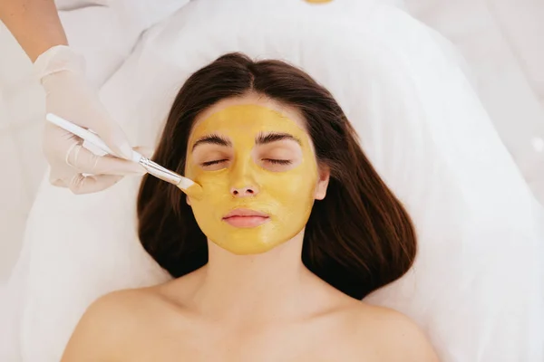 美容師は女性の顔に顔の金のマスクを適用します 美容室で美容と顔のスキンケア 金のマスクだ 化粧品手順 — ストック写真