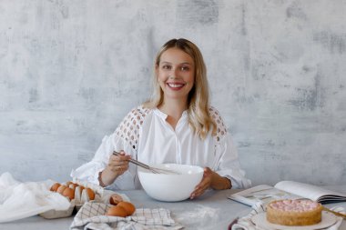 Beyaz bir karıştırma kabında çırpılmış kremayla gri arka planda çırpılan bir kadın..