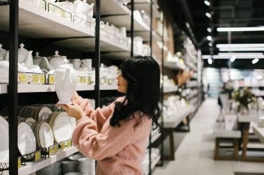 Pembe kazaklı esmer bir kadın bir mağazadan yemek takımı alıyor..