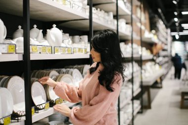 Pembe kazaklı esmer bir kadın bir mağazadan yemek takımı alıyor..