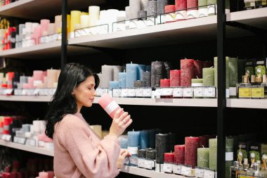 Pembe kazaklı esmer bir kadın mağazadan dekoratif bir mum alıyor..