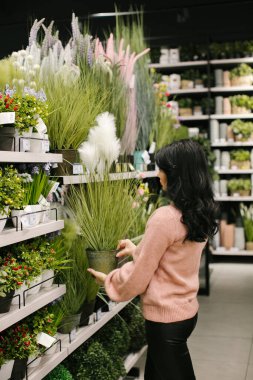 Pembe kazaklı esmer bir kadın mağazadan süslü saksılar alıyor..