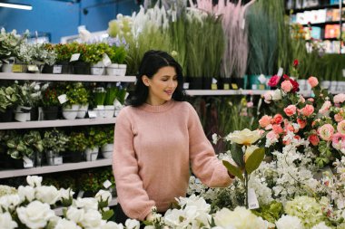 Pembe kazaklı esmer bir kadın mağazadan süslü saksılar alıyor..