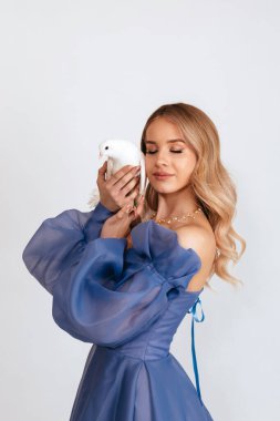 Mavi kabarık elbiseli mutlu genç kadın beyaz arka planda barışın beyaz güvercin sembolünü tutuyor. Boşluğu kopyala.