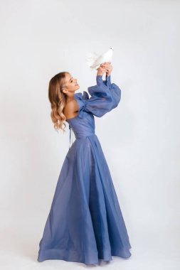 Mavi kabarık elbiseli mutlu genç kadın beyaz arka planda barışın beyaz güvercin sembolünü tutuyor. Boşluğu kopyala.