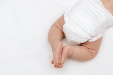 Newborn baby legs in a white nappy on the bed. Top view. Baby skin care and diaper change.