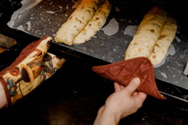 A woman puts a baking sheet with traditional German Christmas bread Stollen into the oven. clipart