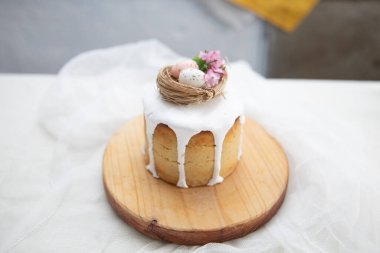 Beyaz jöleli Paskalya pastası. Süslü kuş yuvası. Tahta tahtada yumurta, çiçek ve beyaz gazlı bez..
