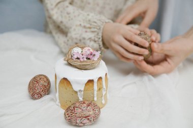 Beyaz jöleli Paskalya pastası. Süslü kuş yuvası, yumurta ve çiçeklerle. Ahşap elle boyanmış Paskalya yumurtaları ellerinde.