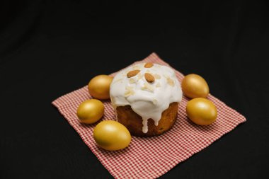 Beyaz kremalı Paskalya pastası ve siyah arka planda peçete üzerine badem fıstığı. Sarı ya da altın yumurta. Boşluğu kopyala.