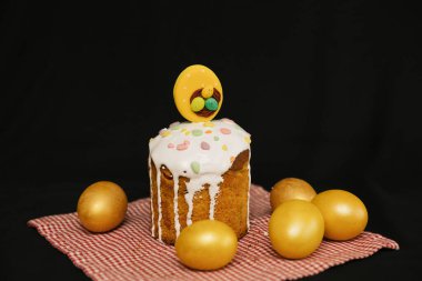 Beyaz kremalı ve renkli süslemeli Paskalya pastası ve siyah arka planda sarı yumurtalar..