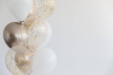 Golden and white balloons and balloons with glitter on white background on the left. Copy space.
