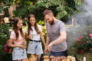 Bahçede aile barbeküsü ızgarası. Barbekü partisi. Bir aile ızgarada eğleniyor ve sohbet ediyor. İki kızla sakallı adam ızgarada sohbet ediyor.. 