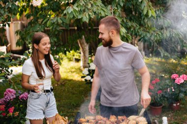 Bahçede aile barbeküsü ızgarası. Barbekü partisi. Bir aile ızgarada eğleniyor ve sohbet ediyor. Kız kardeşiyle sakallı adam ızgarada sohbet ediyor.. 