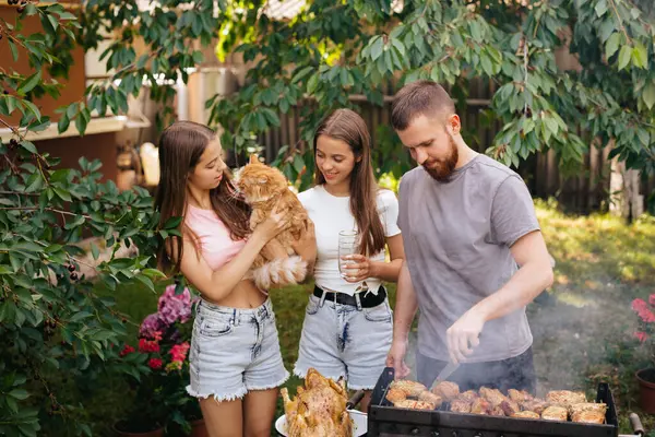 stock image Family barbecue grill in the garden. Barbecue party. A family with a ginger cat is having fun and chatting on the grill.Bearded man with two girls are chatting on the grill. 