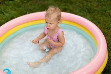 Pembe mayo giyen mutlu bebek yüzüyor ve arka bahçede şişme havuzda oyuncaklarla oynuyor. Yaşam biçimi. 