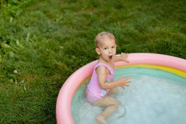 Pembe mayo giyen bebek arka bahçede şişme havuzda yüzüyor.. 