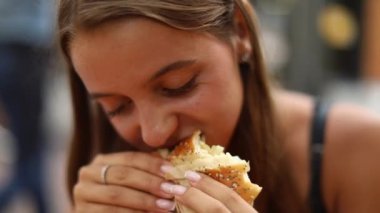 Dışarıda hamburger yiyen, uzun saçlı, bronzlaşmış genç bir kadın. Yaşam tarzı kavramı. 
