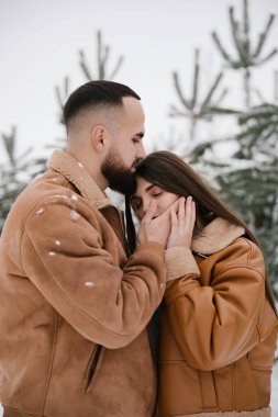 Kahverengi ceketli çift kışın sarılıyor. Yüzler birbirine yakın..