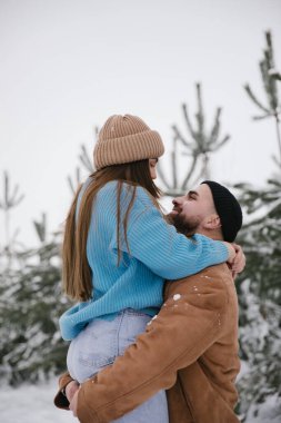 Sevdiği kadını kollarında tutan bir adam. Mutlu çift kışın karlı ormanda vakit geçiriyor..
