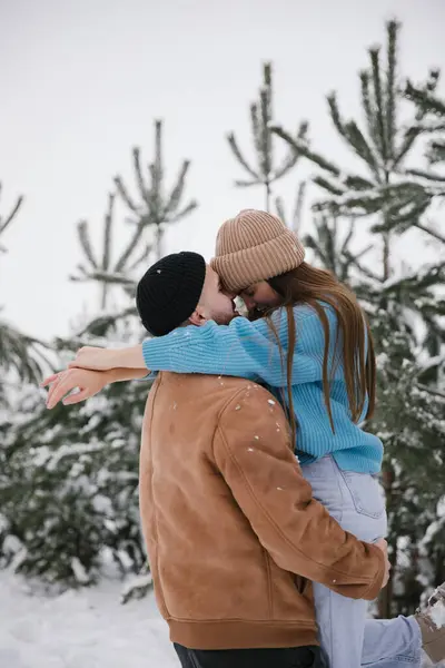 stock image A man holding his beloved woman in his arms. Happy couple spending time in winter in snowy forest.