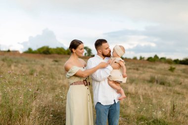 Doğada bebeği olan bir aile. Nane rengi elbiseli bir kadın ve beyaz etekli sakallı bir adam, tarlada bej elbiseli yeni doğmuş bir kıza sarılıyorlar. Aile, yaşam tarzı konsepti.