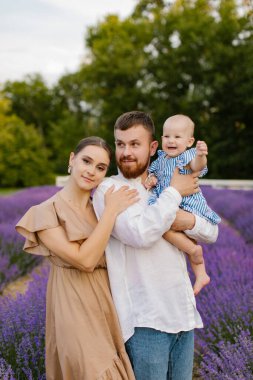 Lavanta tarlasında bebekli bir aile. Kahverengi elbiseli bir kadın ve sakallı beyaz etekli bir adam lavanta tarlasında mavi elbiseli yeni doğmuş bir kızı tutuyorlar. Aile, yaşam tarzı konsepti.