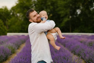 Beyaz gömlekli sakallı bir adam lavanta tarlasında bebek kaldırıyor. Baba kızını kaldırıyor ve eğleniyor..