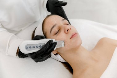 Genç kız dermatolog tarafından ultrasonik yüz temizleme tedavisi görüyor. Gençlerin yüzünde ultrasonik yüz temizleme. Genç teni.