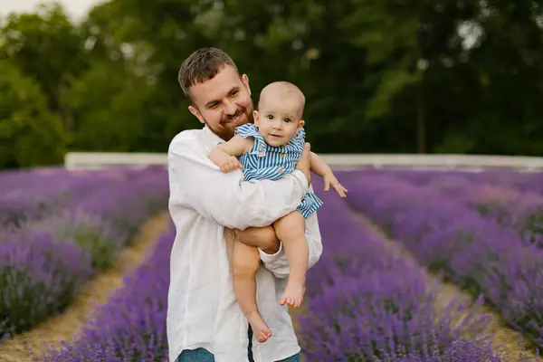 stock image A bearded man in a white shirt is lifting baby in air on a lavender field. Daddy is lifting up daughter and have fun.