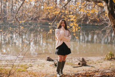 Uzun saçlı, bej kazaklı, siyah etekli ve lastik çizmeli genç bir kadın sonbaharda ormanda dans ediyor..