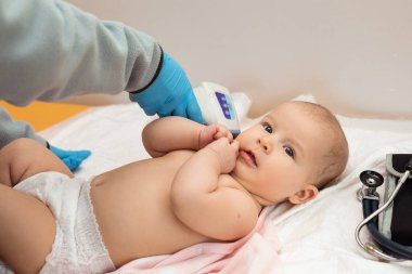 Bir çocuk doktoru 6 aylık bir bebeğin ısısını dijital kızılötesi termometreyle ölçüyor. Aşıdan önce bebeğin muayenesi. 