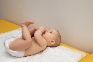 A little baby in a diaper is lying on back on the couch and sucking his toe. clipart