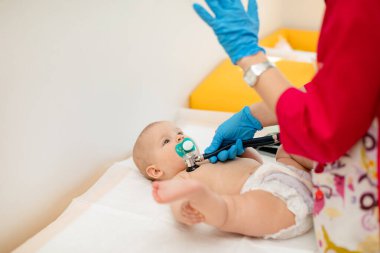 Pediyatrist hastanede yeni doğmuş bir bebeği muayene ediyor. Çocuk doktoru bebeğin kalp atışlarını dinlemek için steteskop kullanıyor..