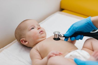 Çocuk doktoru, bebeğini muayene ediyor. Çocuğun kalp atışlarını dinlemek için steteskop kullanan bir doktor. Kapat..