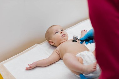 Çocuk doktoru, bebeğini muayene ediyor. Çocuğun kalp atışlarını dinlemek için steteskop kullanan bir doktor. Kapat..